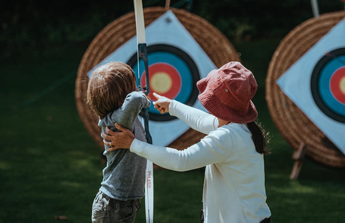 Woman guides boy in archery
