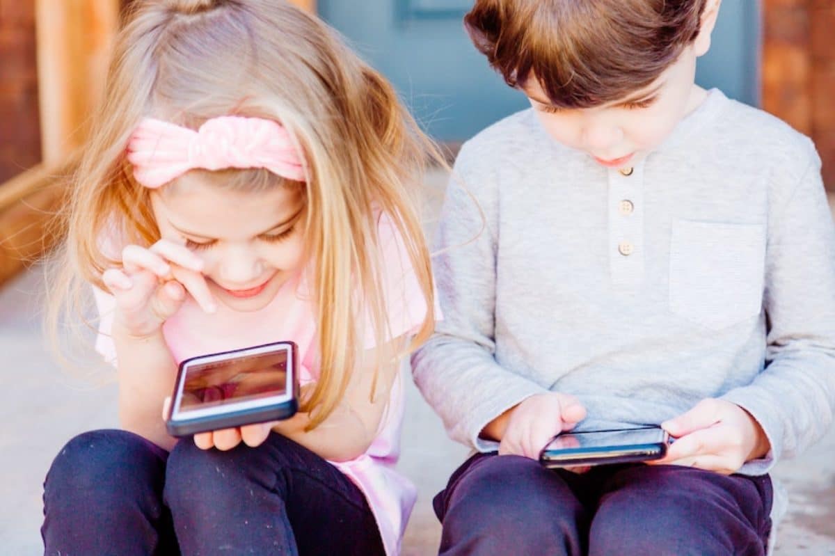 Two children mesmerized by smartphones